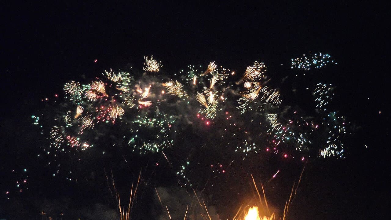Fireworks bursting in white, gold and red over a dark night sky with a bonfire glowing at the bottom, at Lewes on Bonfire Night in 2013